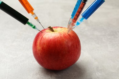 Photo of GMO concept. Red apple with different syringes on grey textured table, closeup