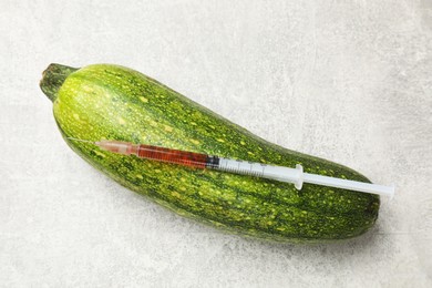 Photo of GMO concept. Zucchini and syringe with liquid on grey textured table, top view