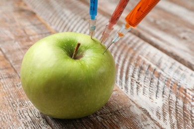 Photo of GMO concept. Green apple with syringes on rustic wooden table, closeup