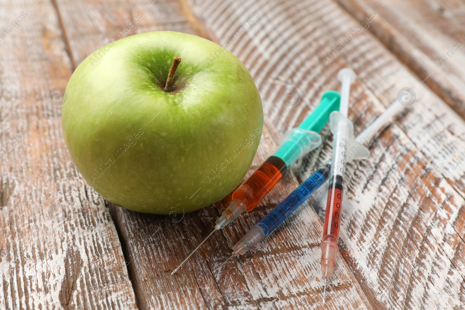 Photo of GMO concept. Green apple and syringes on rustic wooden table, closeup