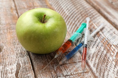 Photo of GMO concept. Green apple and syringes on rustic wooden table, closeup