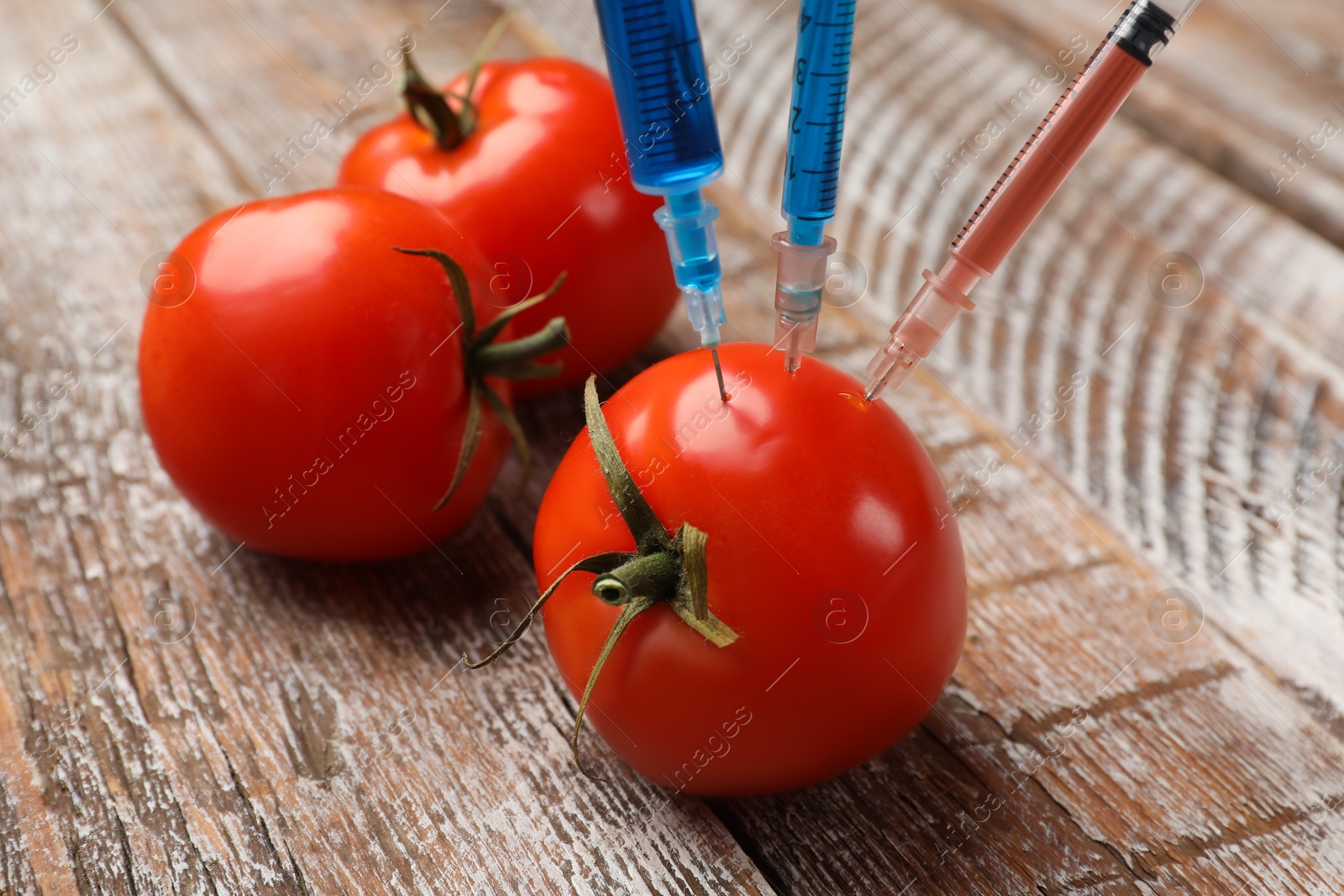 Photo of GMO concept. Tomato with syringes on rustic wooden table, closeup