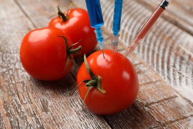 Photo of GMO concept. Tomato with syringes on rustic wooden table, closeup