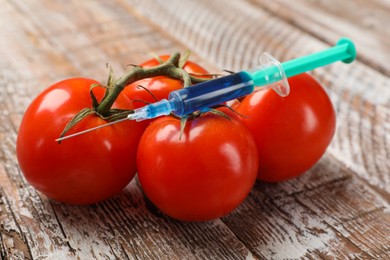 Photo of GMO concept. Tomatoes and syringe on rustic wooden table, closeup