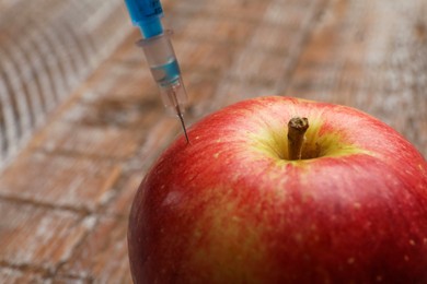 Photo of GMO concept. Injecting apple with syringe on blurred background, closeup