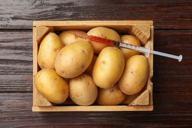 Photo of GMO concept. Potatoes in crate and syringe with liquid on wooden table, top view