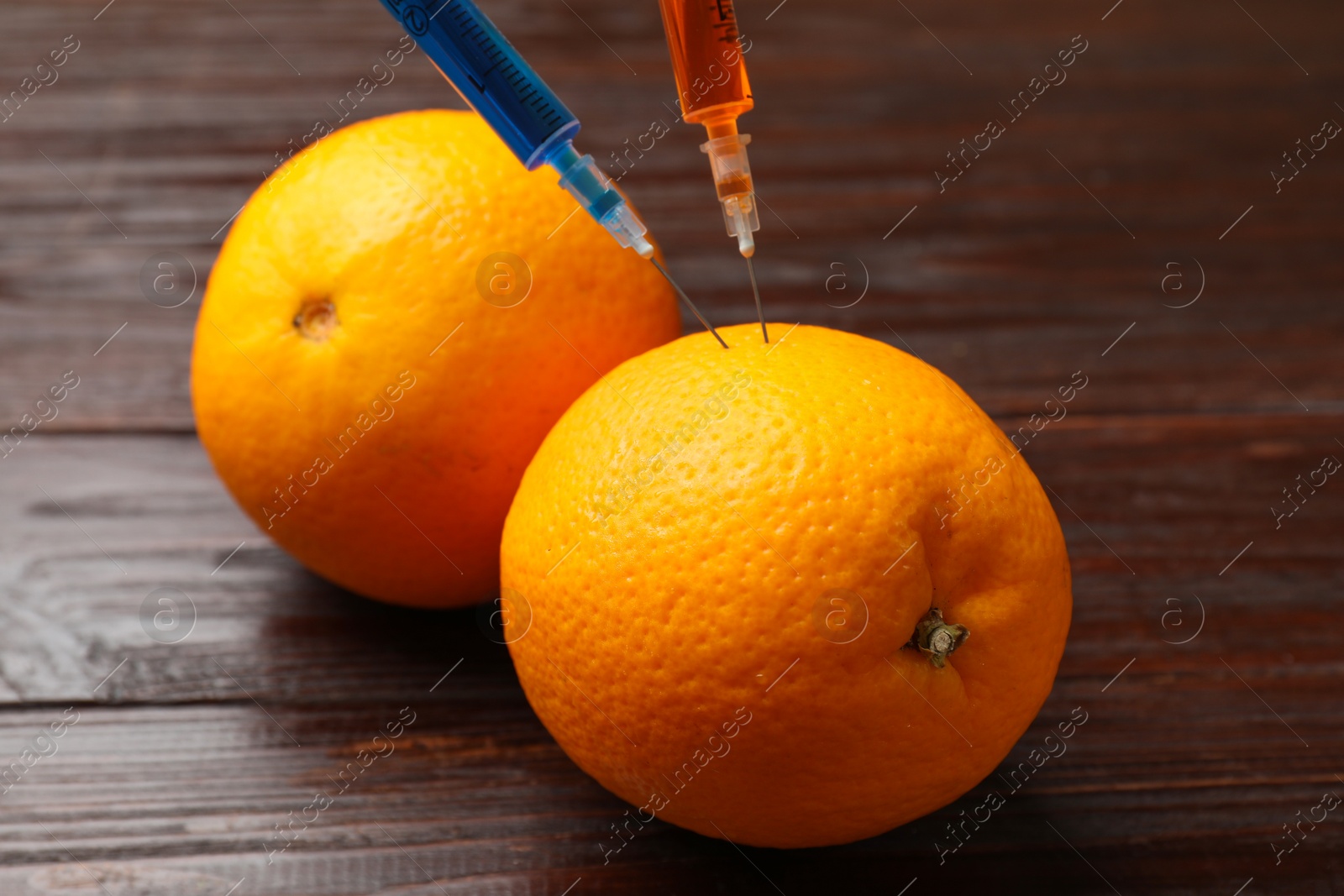 Photo of GMO concept. Orange with syringes on wooden table, closeup