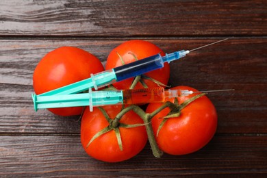 Photo of GMO concept. Tomatoes and syringes on wooden table, flat lay