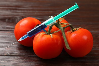 Photo of GMO concept. Tomatoes and syringe on wooden table, closeup