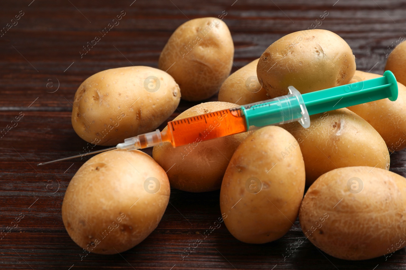 Photo of GMO concept. Potatoes and syringe on wooden table, closeup