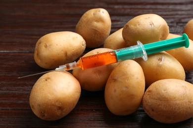 Photo of GMO concept. Potatoes and syringe on wooden table, closeup