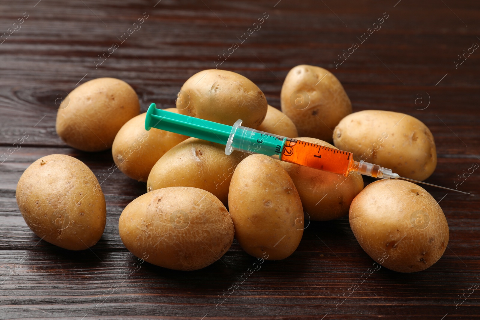 Photo of GMO concept. Potatoes and syringe on wooden table, closeup