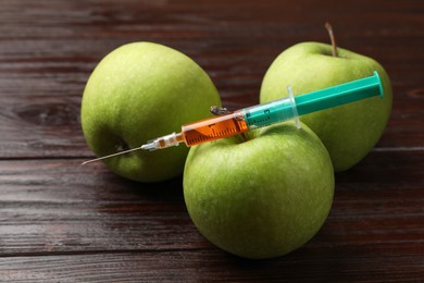 Photo of GMO concept. Green apples and syringe on wooden table, closeup