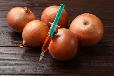 Photo of GMO concept. Onion bulbs and syringe on wooden table, closeup