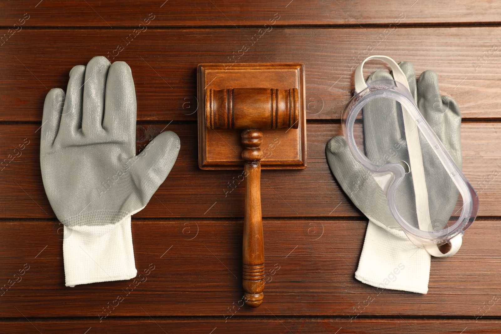 Photo of Accident at work concept. Gavel, protective gloves and goggles on wooden table, flat lay