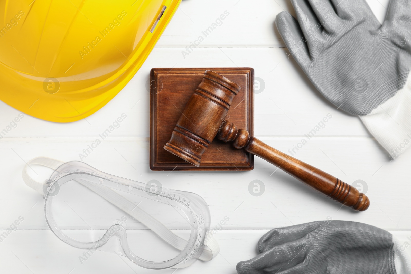 Photo of Accident at work concept. Gavel and protective gear on white wooden table, flat lay