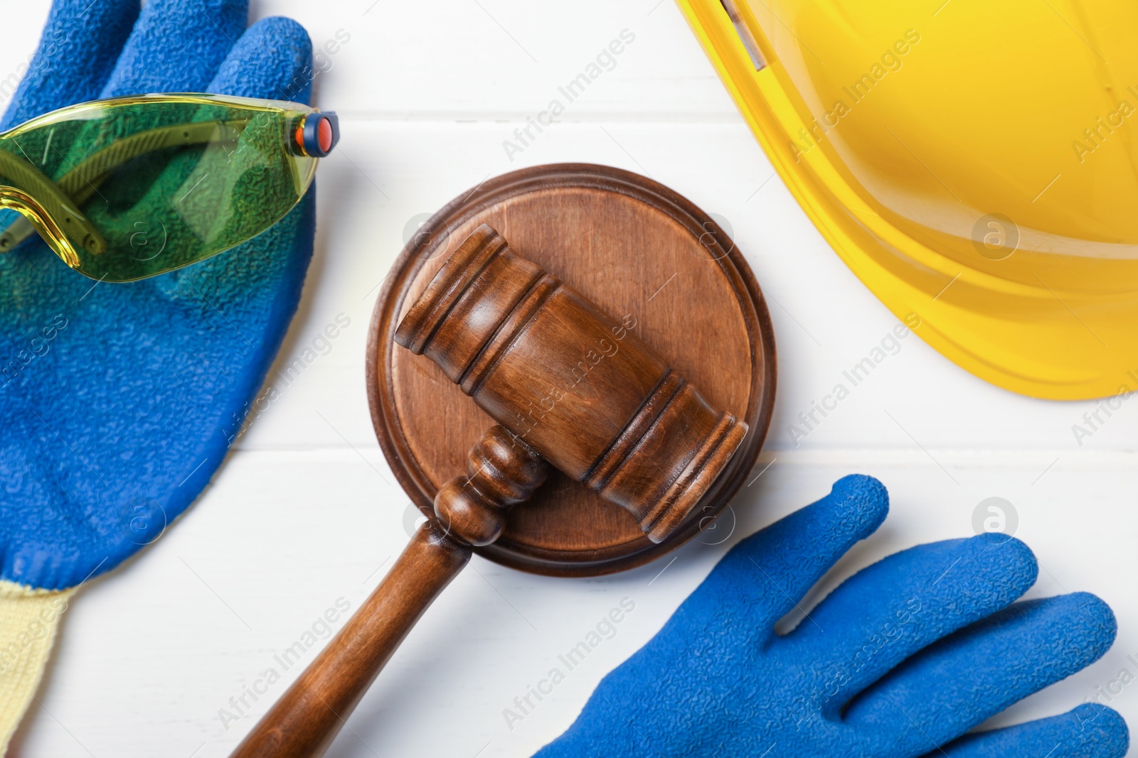 Photo of Accident at work concept. Gavel and protective gear on white wooden table, flat lay