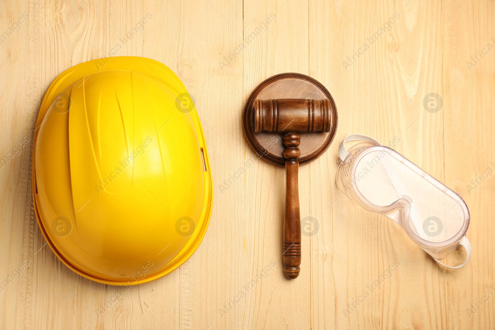 Photo of Accident at work concept. Gavel, hardhat and protective goggles on wooden table, flat lay