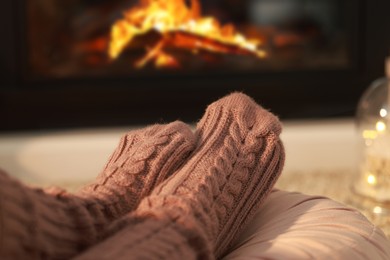 Photo of Woman in knitted socks resting near fireplace at home, closeup