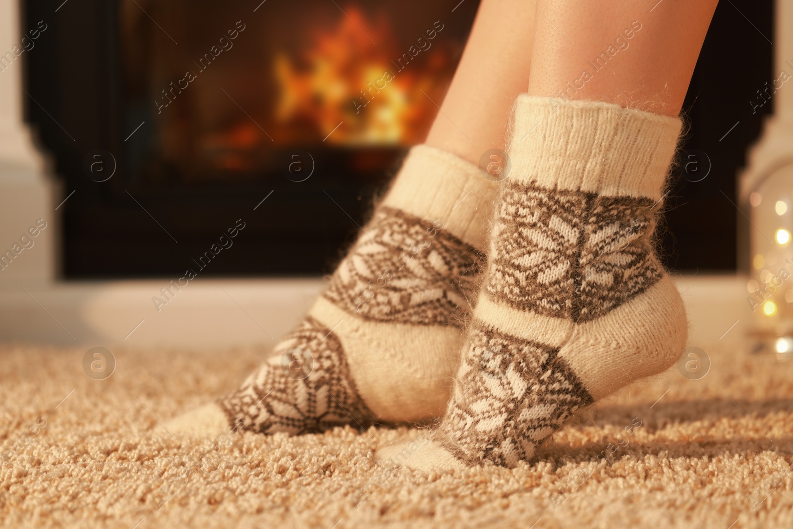 Photo of Woman in warm socks resting near fireplace at home, closeup