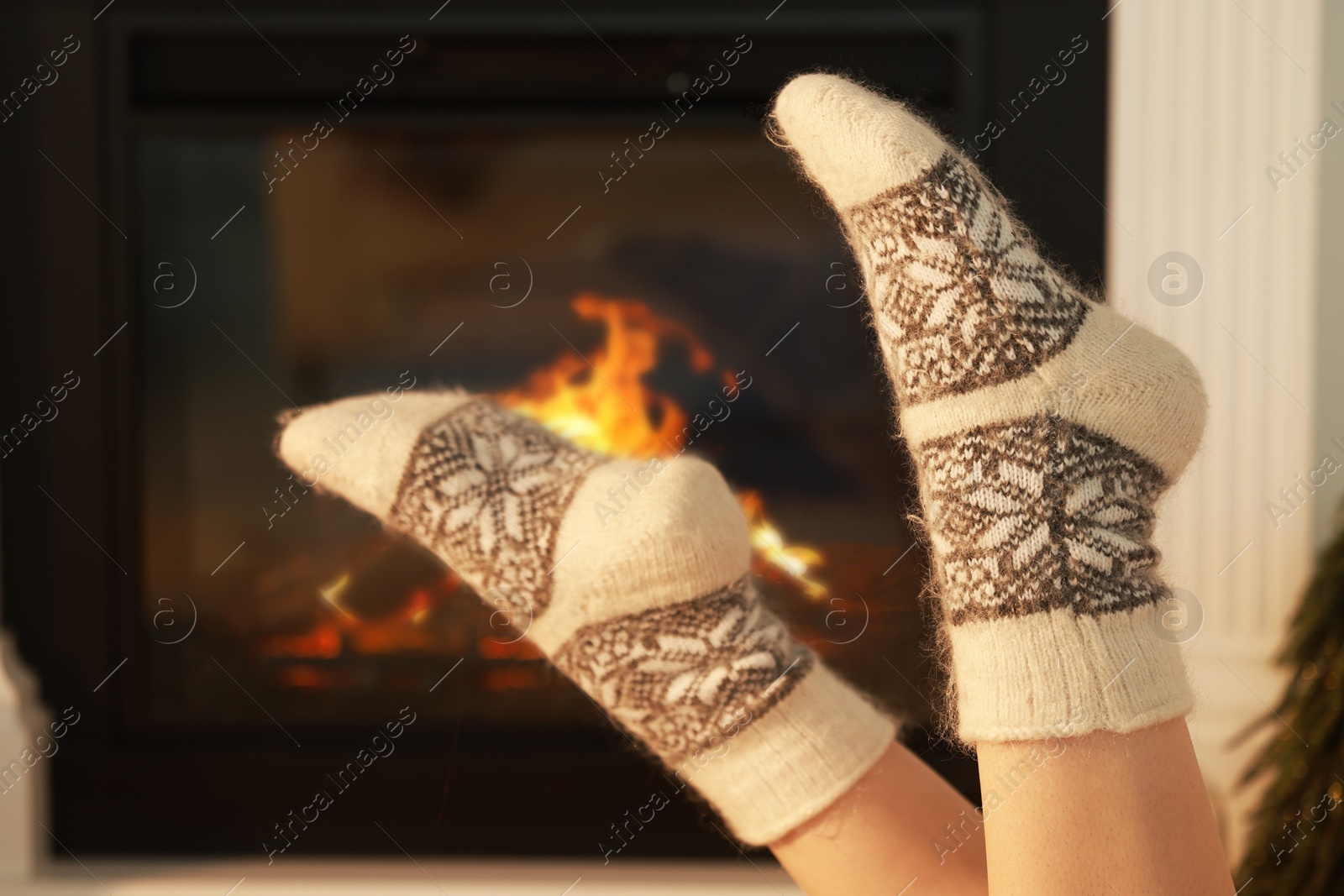 Photo of Woman in warm socks resting near fireplace at home, closeup