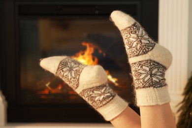 Photo of Woman in warm socks resting near fireplace at home, closeup