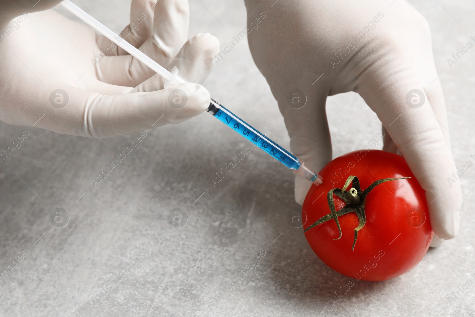 Photo of GMO concept. Scientist injecting something into fresh tomato at grey table, closeup