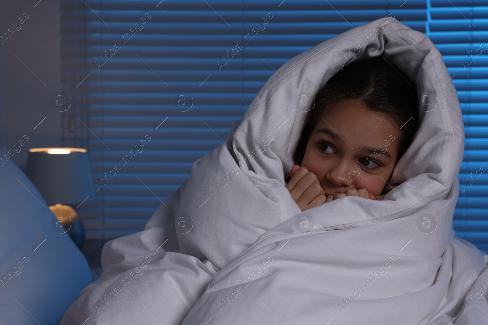 Photo of Afraid girl wrapped in duvet on bed at night. Space for text