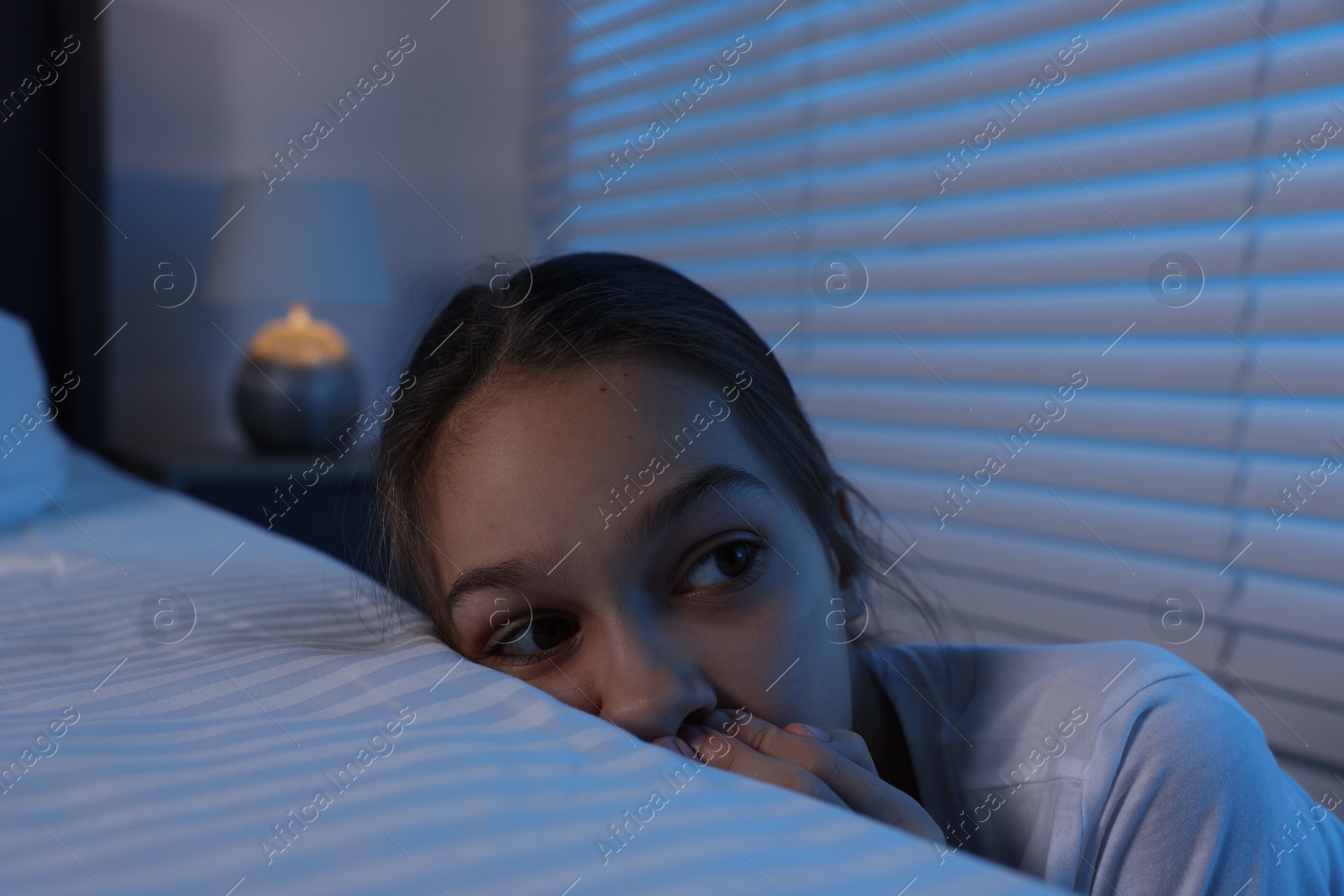 Photo of Scared girl hiding behind bed at night