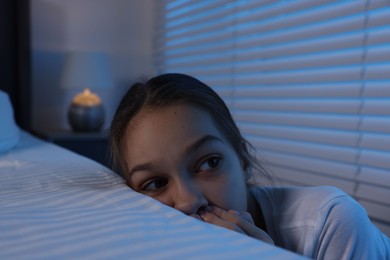 Scared girl hiding behind bed at night