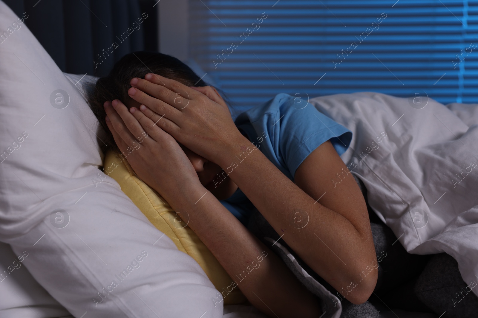 Photo of Scared girl covering face with hands in bed at night