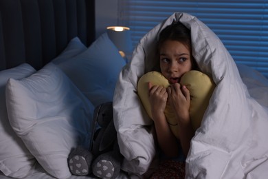 Photo of Afraid girl with pillow under duvet on bed at night