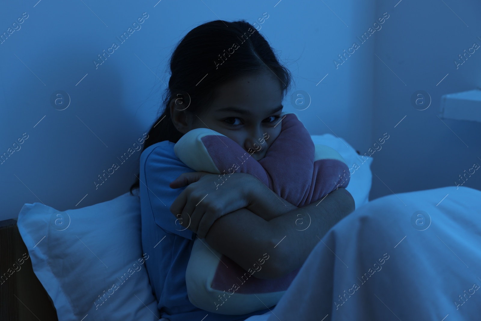 Photo of Afraid girl with pillow in bed at night