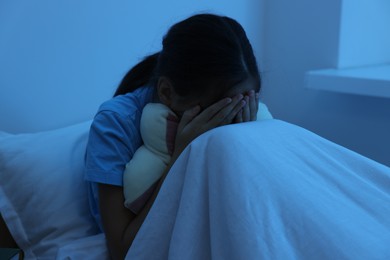 Photo of Afraid girl covering face with hands in bed at night