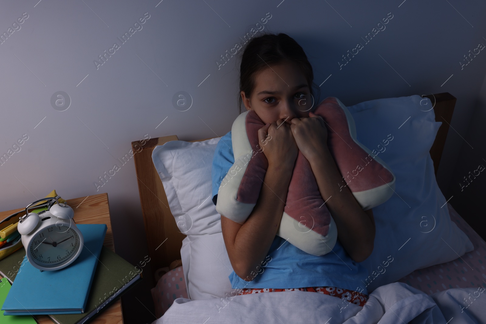 Photo of Afraid girl with pillow in bed at night