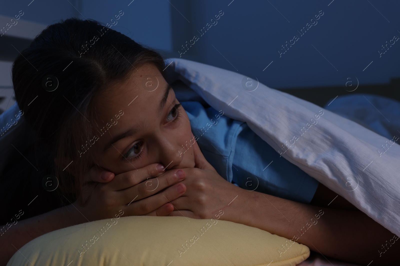 Photo of Afraid girl with pillow under duvet on bed at night