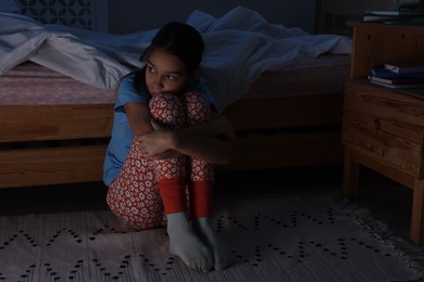 Afraid girl near bed in her room at night. Space for text