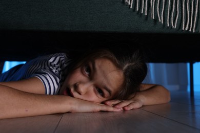 Fearful girl hiding under bed at night