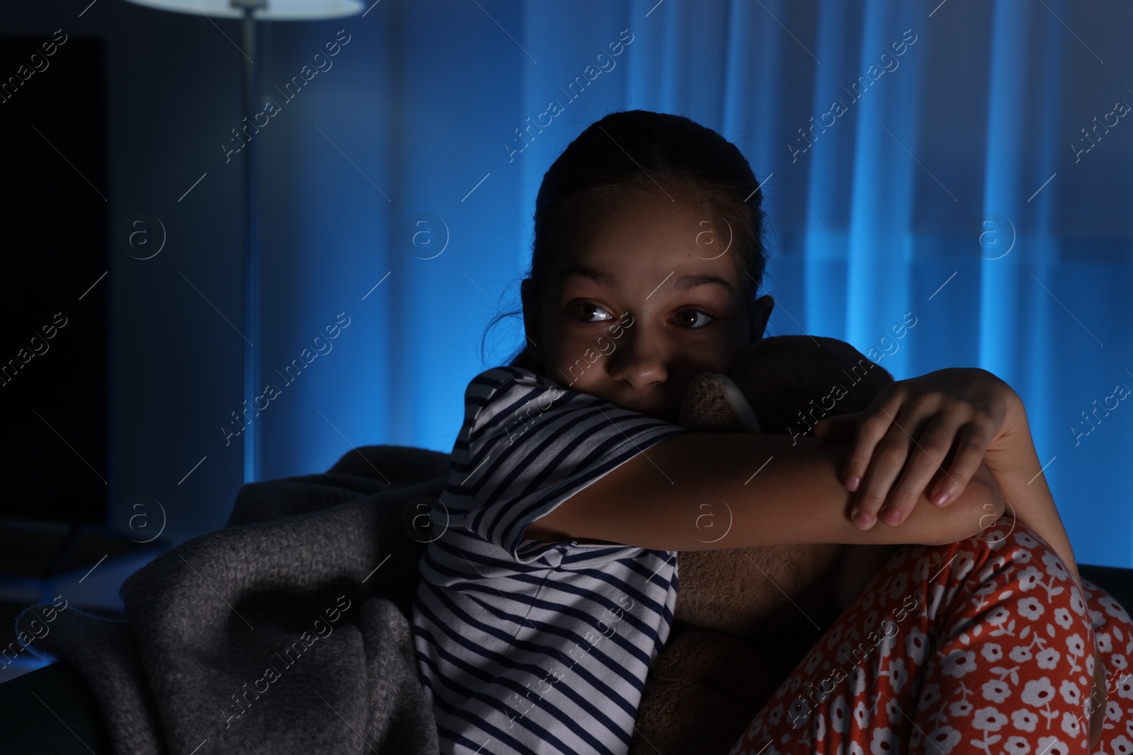 Photo of Afraid girl with teddy bear on sofa at home