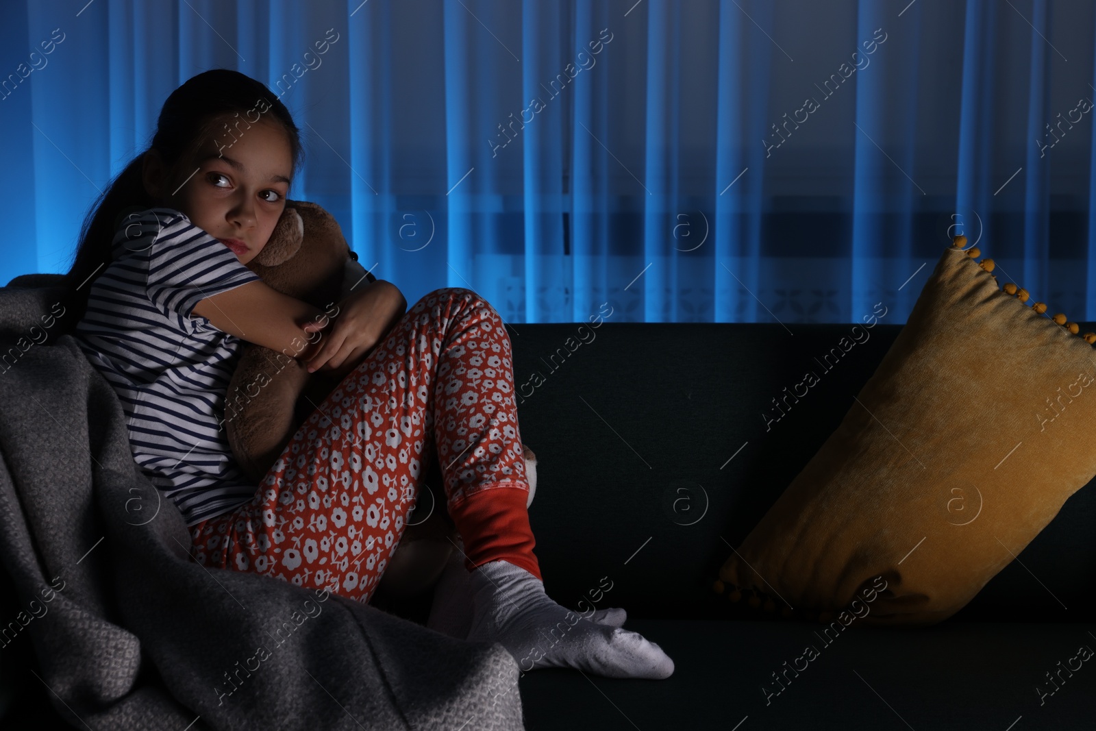 Photo of Afraid girl with teddy bear on sofa at home. Space for text