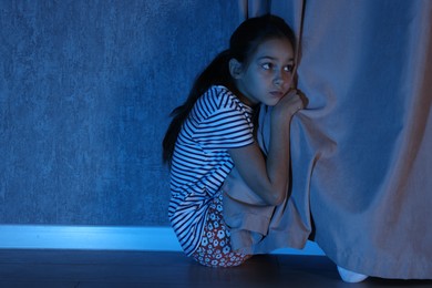 Scared girl hiding behind curtain at night. Space for text