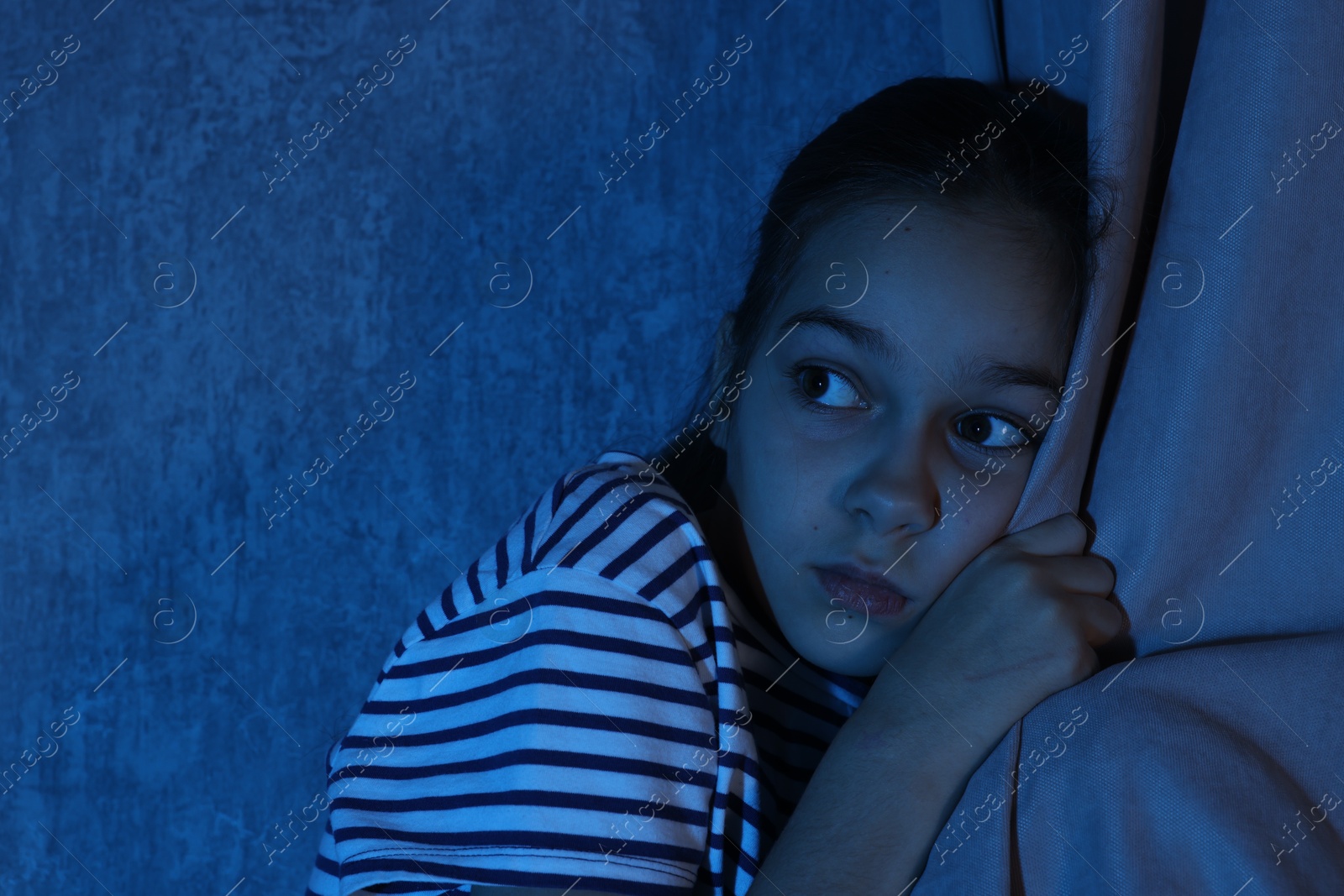 Photo of Scared girl hiding behind curtain at night. Space for text