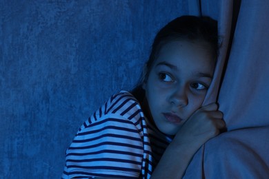 Scared girl hiding behind curtain at night. Space for text