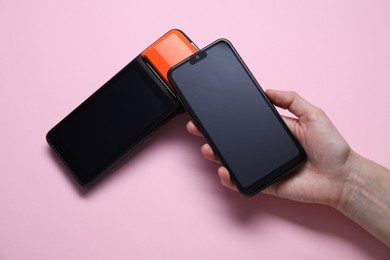 Photo of Woman with smartphone using payment terminal on pink background, top view