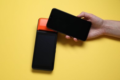 Photo of Woman with smartphone using payment terminal on yellow background, top view