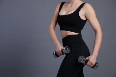 Photo of Woman in sportswear exercising with dumbbells on grey background, closeup. Space for text