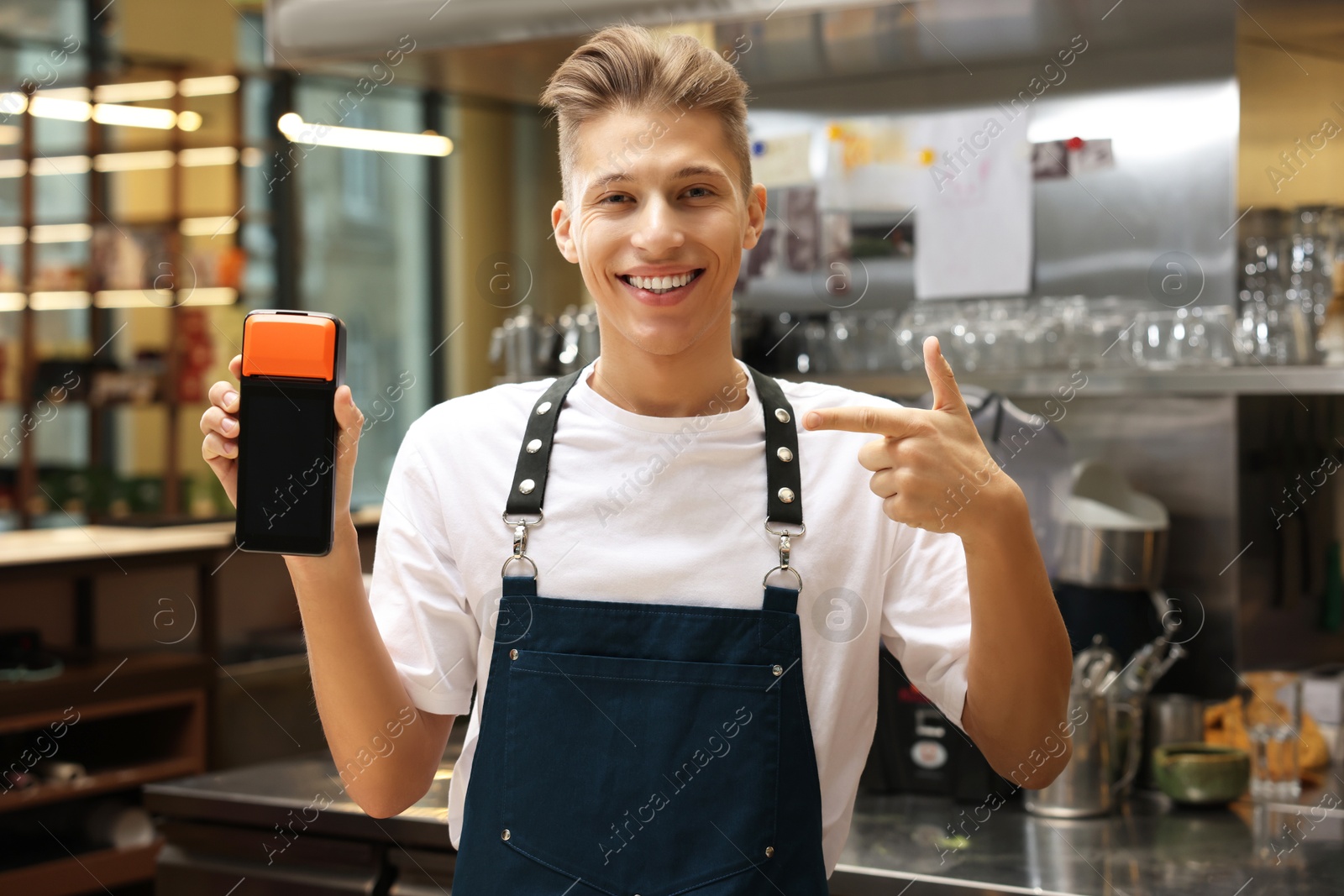 Photo of Smiling cafe worker pointing at payment terminal indoors