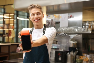 Photo of Smiling cafe worker with payment terminal indoors