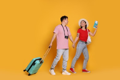 Happy travellers with passports and suitcase on yellow background