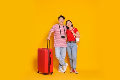 Happy travellers with suitcase on yellow background